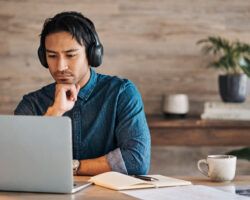 Businessman, headphones and laptop webinar in office with coffee on table, video call or watching video. Zoom call, video conference and male from Canada in online meeting with book and pen on desk.