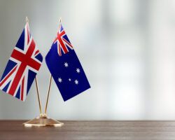 Australian And British Flag Pair On A Desk Over Defocused Background