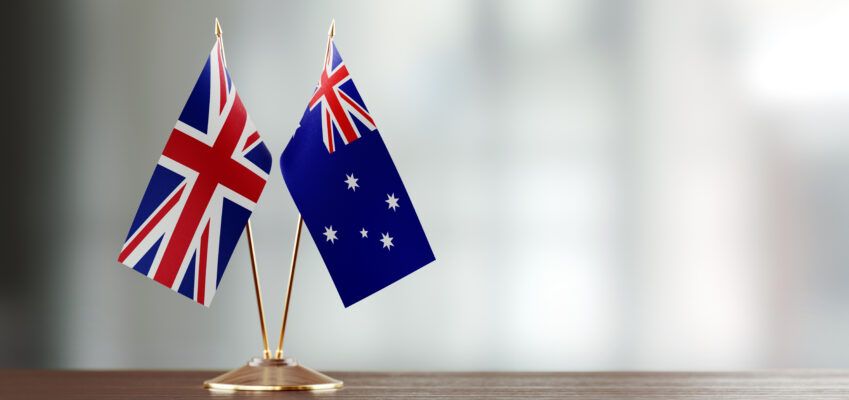 Australian And British Flag Pair On A Desk Over Defocused Background